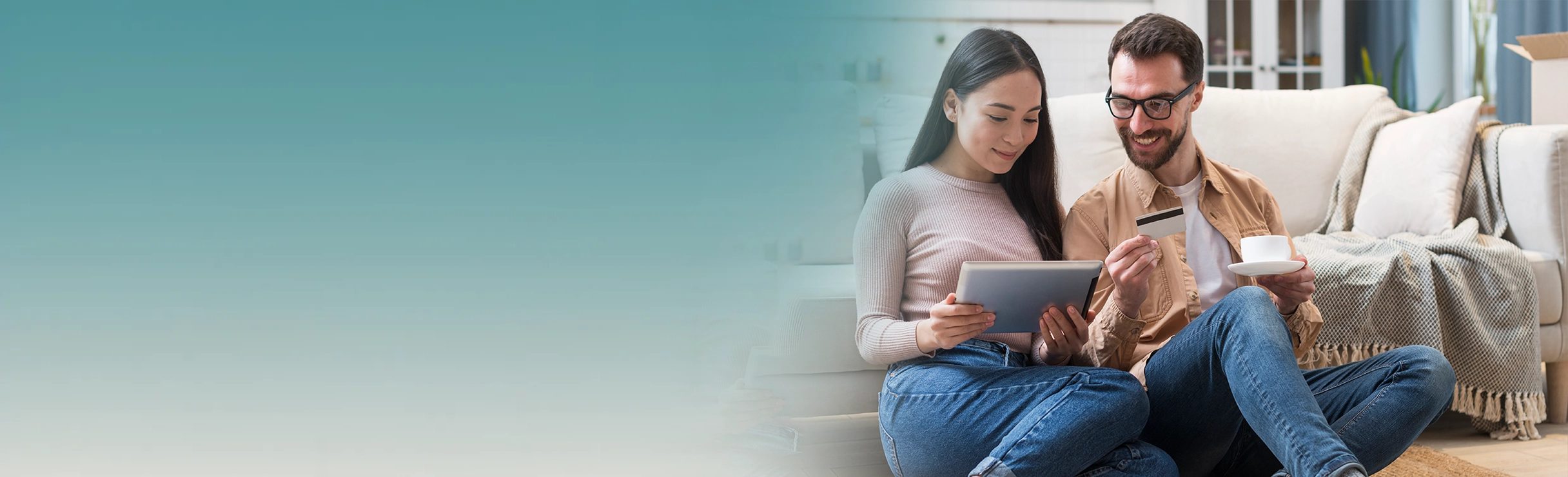 A smiling couple at home looking at a tablet together, one holding a payment card